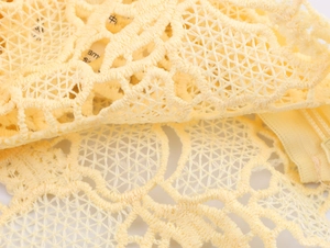 Detailed close-up of yellow floral lace fabric with intricate hollow embroidery patterns