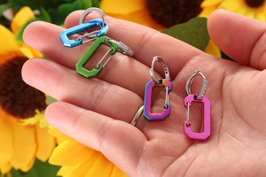 Detail of colorful carabiner drop earrings with pavé zircon hoops held in hand
