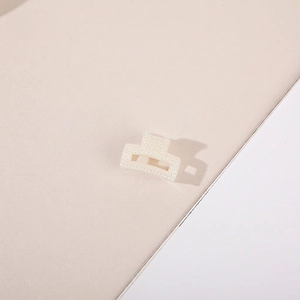 Close-up of a hollow rectangular hair claw clip decorated with cream pearls on a geometric base