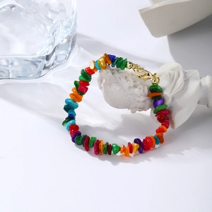 Close-up of rainbow bohemian stone bead bracelet with a gold lobster clasp on white desk