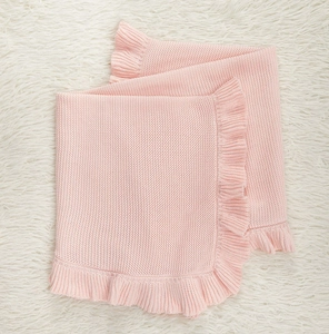 Detailed knit texture of pink baby blanket with delicate ruffled edges on plush background