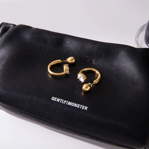 Detail of 18K gold stainless steel C-shape earring with oval zircon on black leather