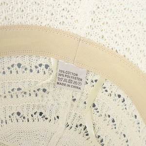 Detail view showing a white knit sun hat with a beige sweatband and composition label