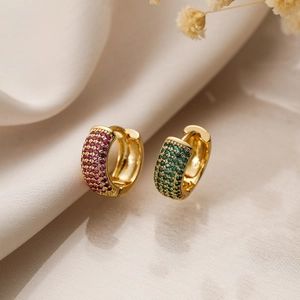 Macro shot of gold-plated hoop earrings with vibrant pink and green zircon stones on silk