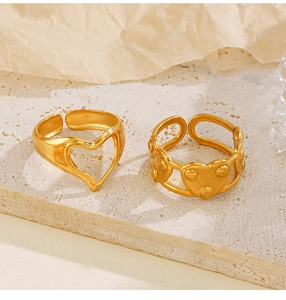 Detailed close-up of gold-plated heart-shaped open rings on natural stone texture