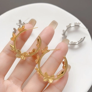 Close-up of gold and silver butterfly hoop earrings held over a white plate