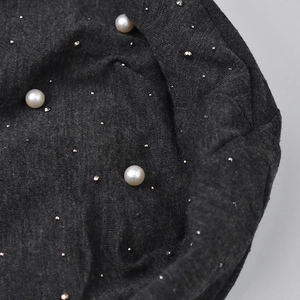 Detailed macro view of dark grey knit fabric with white pearls and silver metal studs