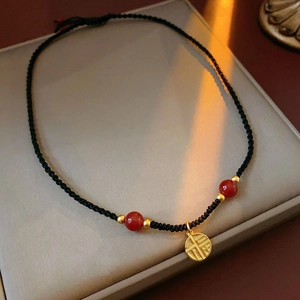 Detail of hand-woven black cord necklace with red bead and golden Fu character pendant