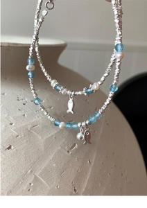 Detail of silver beads and pearl bracelet with a minimalist fish charm and blue beads