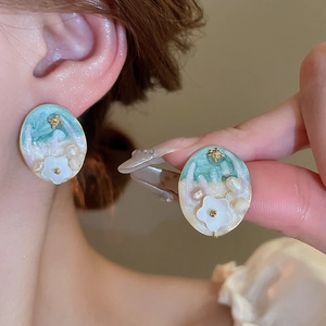 Detailed view of vintage-style pearl flower stud earrings with green enamel and gold finish