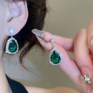 Detail of luxury teardrop green crystal earrings with diamond halo worn by model