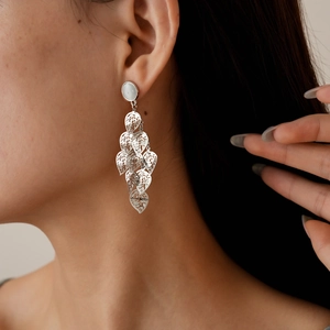 Macro view of silver leaf-shaped tassel earrings with cat-eye stones on a model