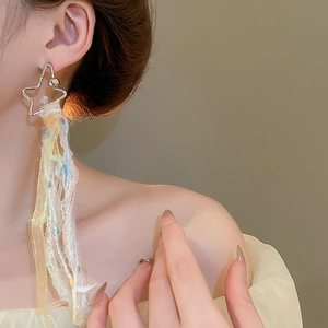 Détail de boucles d'oreilles étoile avec pompons en ruban coloré portées par un mannequin
