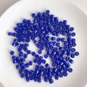Close-up of glossy deep blue cylindrical acrylic beads scattered on a white ceramic plate