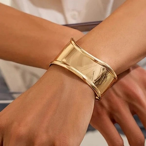 Close-up of a wide gold-plated stainless steel cuff bracelet with asymmetrical design