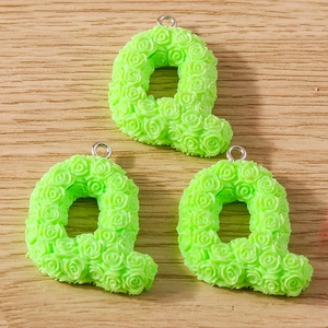 Macro detail of three green Q-shaped resin charms with rose texture and metal rings