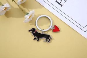 Detail view of black dachshund keychain with red heart charm on yellow background