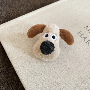 Detailed view of plush beige puppy brooch on aesthetic book with textured fabric
