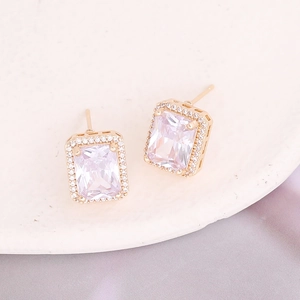 Detail of square zircon stud earrings with gold plating on elegant purple silk fabric