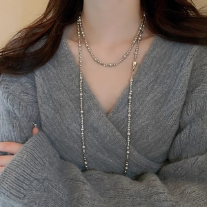 Long collier à billes argentées polies avec crochets en métal sur un pull gris