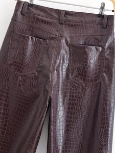 Macro view of dark brown crocodile-embossed leather trousers showing back pockets and waist