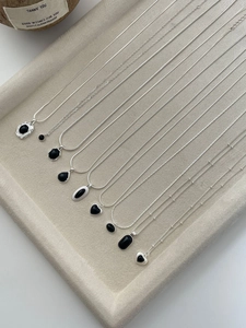 Detailed flat lay of silver necklaces with black agate pendants on a beige velvet tray