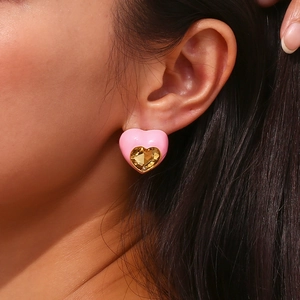 Gros plan de boucles d'oreilles cœur en émail rose avec pierre dorée sur l'oreille du modèle