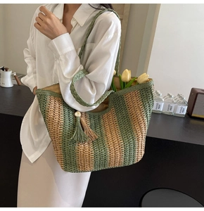 Close-up of green and wood-toned striped straw tote bag with tassel and dual handles