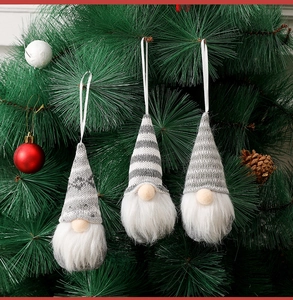 Close-up of three knitted Christmas gnomes hanging on a tree with festive pine cones