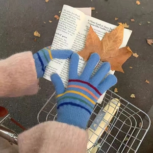 Detail of colorful striped knitted touch screen gloves held against autumn scenery background