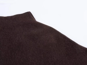 Gros plan sur la texture en tricot marron foncé et le col rond de cette veste cape chic