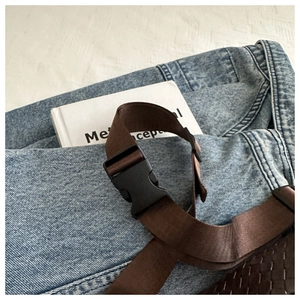 Detail of dark brown woven chest bag with nylon strap and buckle on denim background