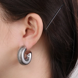 Close-up of silver hollow C-shaped hoop earring with textured ribbing on female model