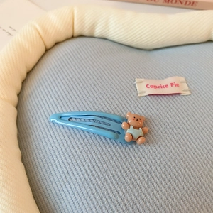 Détail d'une pince à cheveux bleu ciel avec un ours 3D mignon sur tissu bleu