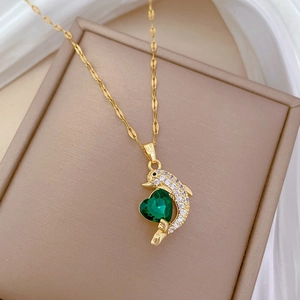 Macro detail of golden dolphin pendant necklace with green heart gem and white crystals