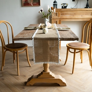 Detail of jute table runner with white pompom fringe on a vintage wooden table setup