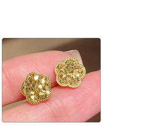 Makroaufnahme goldener Ohrstecker in Blumenform mit mattierter Textur und Perlenrand