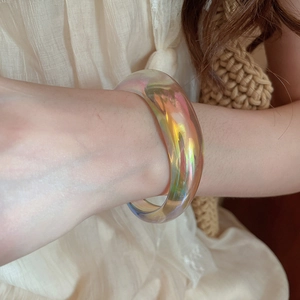 Detail view of a vibrant iridescent acrylic irregular bangle worn on a female wrist.