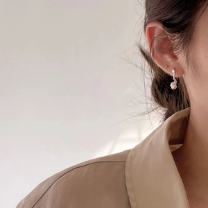 Detailed view of irregular silver drop earrings with spherical charms on a model
