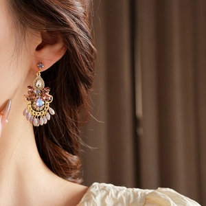 Close-up of golden tassel earrings with purple crystals on a model for a luxury look