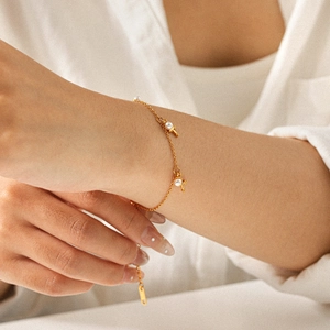 Detailed close-up of gold cross bracelet with elegant white pearls on woman's wrist