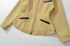 Detail of yellow jacket featuring metallic zipper and black leather patchwork pockets