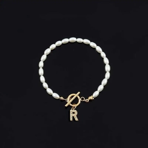 Elegant white oval pearl bracelet with a golden T-bar clasp and rhinestone letter R charm