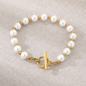 Détail du bracelet en perles d'eau douce et perles dorées avec fermoir OT sur tissu gris
