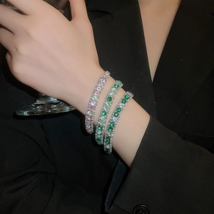Detailed close-up of stacked silver bracelets with colorful zircon stones worn by a model