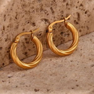 Macro view of gold-plated twisted rope hoop earrings on a textured stone background