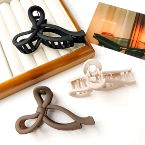 Matte bow hair claws in black, beige and brown colors on a wooden tray and white background