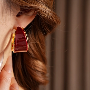 Close-up of vintage gold-plated hoop earring with deep red resin pendant on a model