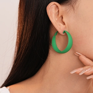 Close-up of a model wearing a matte green large geometric hoop earring with high saturation