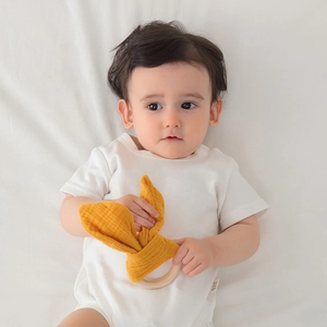 Infant wooden teething ring with yellow fabric bunny ears held by baby on white bedding